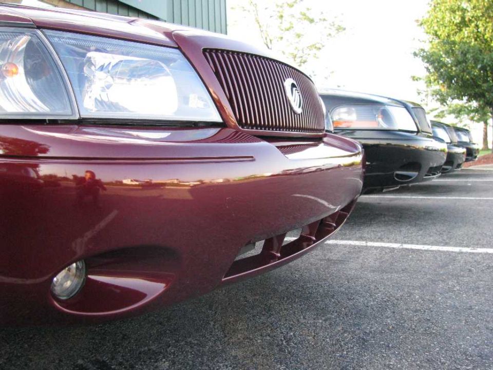 Close-up of a maroon sedan's front bumper and headlight, parked in a lot.