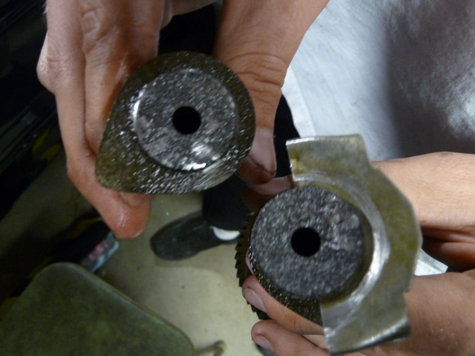 Two metal automotive parts with circular, textured centers and holes, held by hands.
