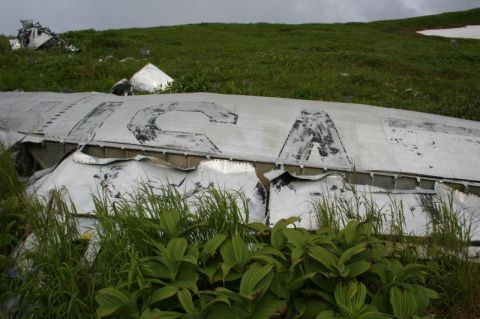 2000 Ford E350 - The image shows the wreckage of an airplane fuselage with the letters "ICA" visible on the side, overgrown with grass and vegetation on a g…