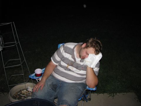 2003 Ford Focus - A man is asleep in a chair with a white cloth over his face. He is wearing a striped shirt and denim shorts. There is a fire pit filled wit…