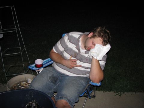 2003 Ford Focus - A man is asleep in a chair outdoors at night, with a paper towel covering his face and a red cup on a holder next to him. A metal ladder an…