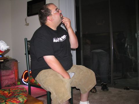 2003 Ford Focus - A man sits in a chair looking up and to the right, with his hand on his chin. He is wearing a black t-shirt and tan shorts. The background…