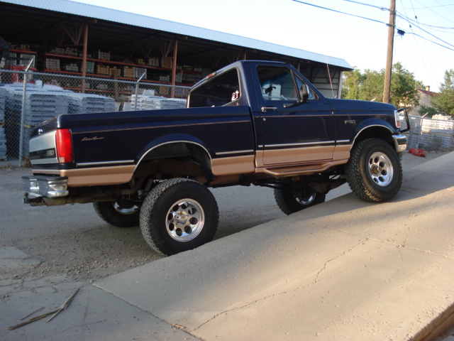 Dark blue Ford F-150 pickup truck with tan trim, lifted suspension, driving up a concrete incline
