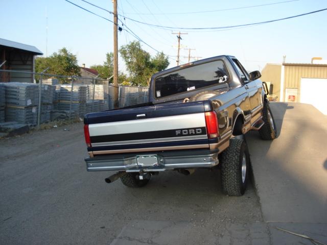 Dark blue Ford pickup truck with silver and tan stripe, lifted suspension, seen from rear