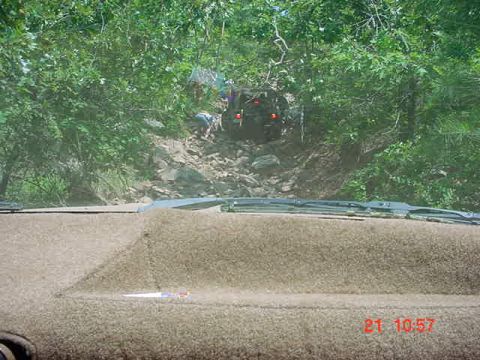 1989 Ford Bronco - A vehicle navigates a challenging off-road trail, ascending a steep, rocky incline amidst dense foliage.