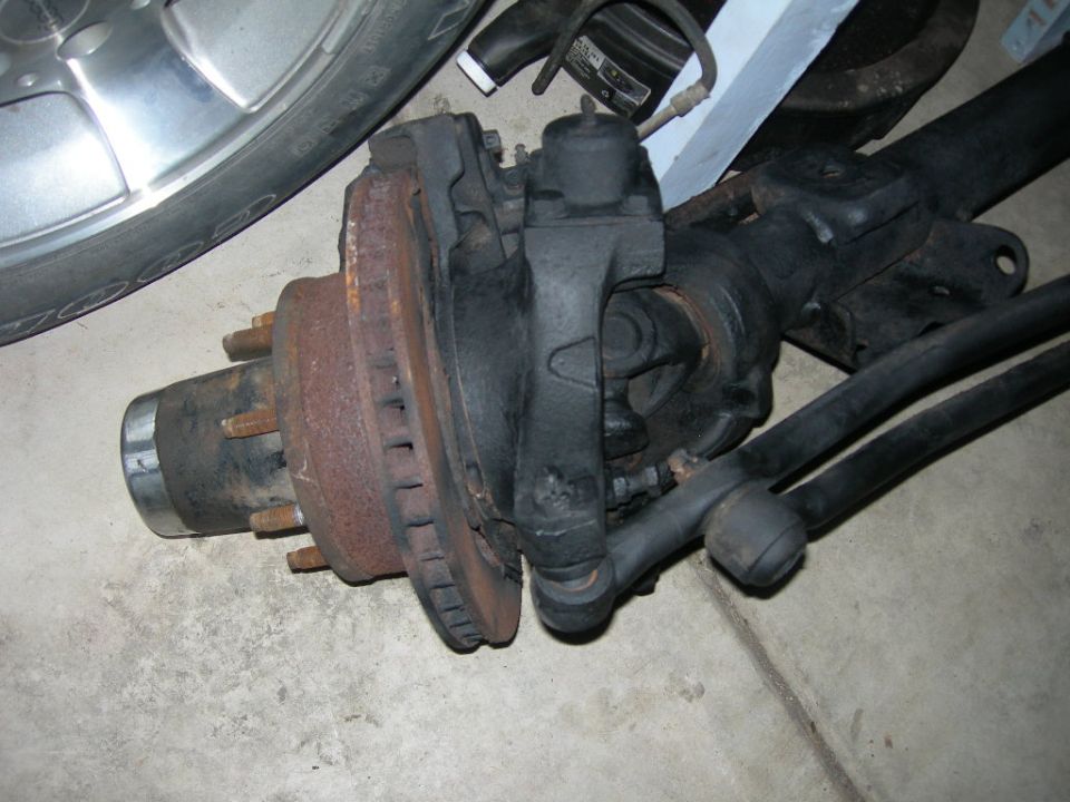 Rusty brake rotor and hub assembly on a black axle with a chrome wheel and tire.