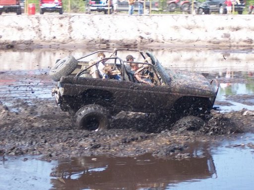 Muddy off-road vehicle with people driving through a mud pit.
