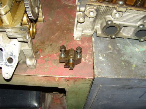 2007 Ford Mustang - Photograph of a small bolted engine part on a workbench beside cylinder heads, not a technical document.