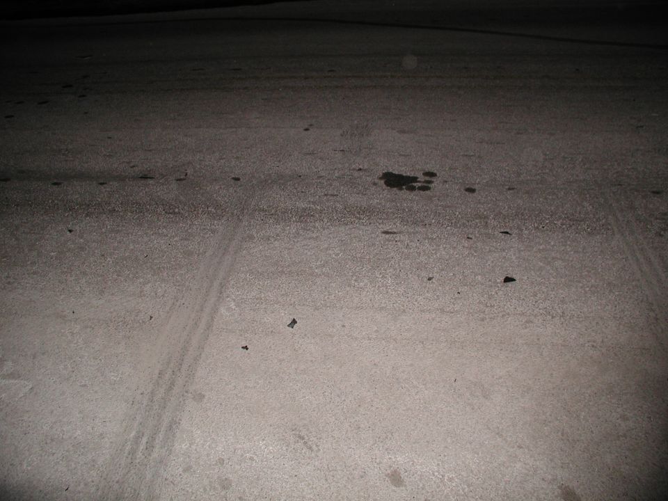Dark pavement at night with faint tire tracks and a small dark fluid stain