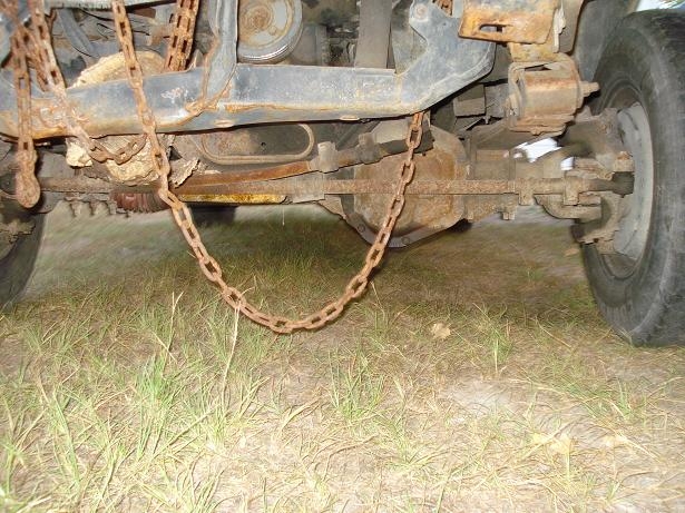 Underside of a rusted vehicle showing differential, drive shaft, and chain.