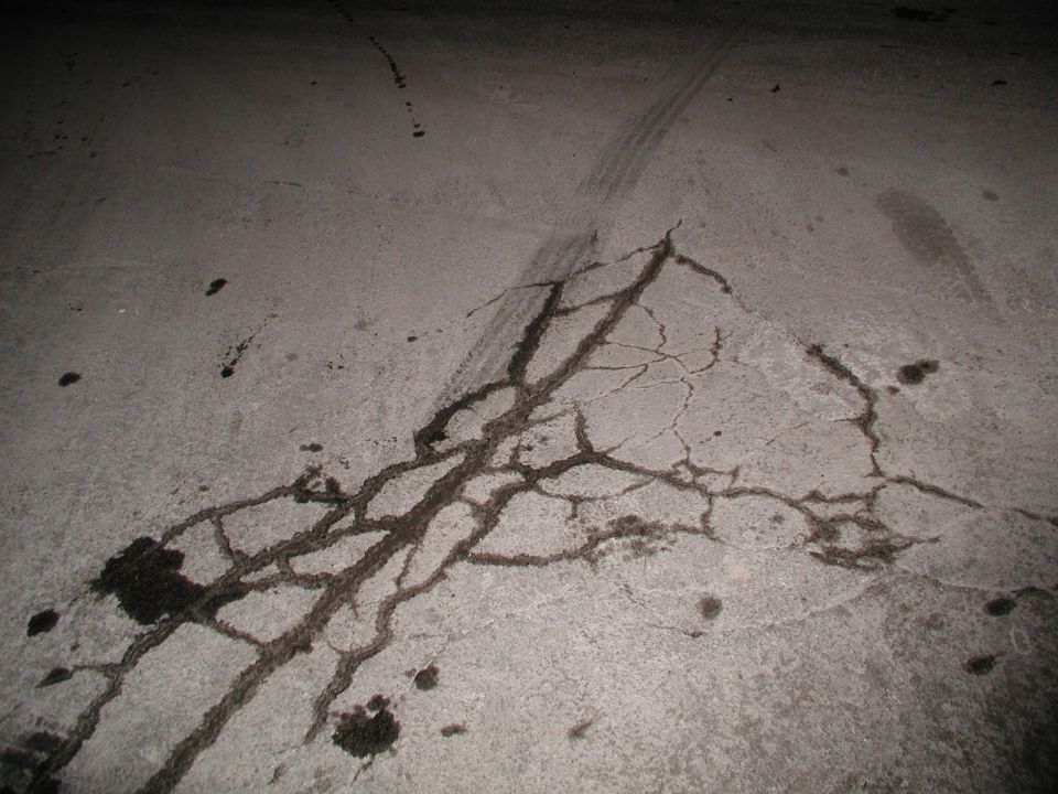 Cracked concrete pavement at night with dark spider-web cracks and scattered debris