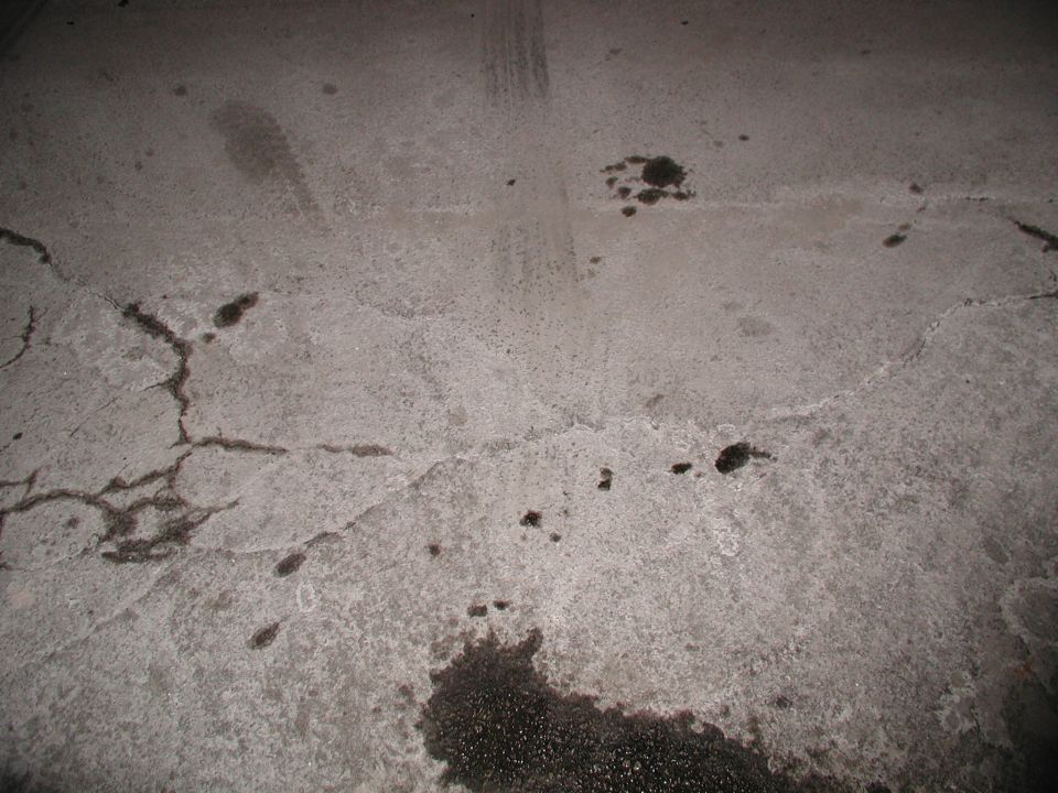 Cracked concrete surface at night with oil stains and dark spots, flash-lit