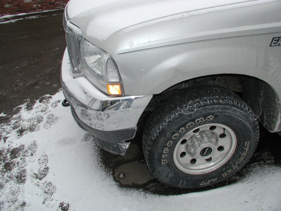 Front corner of silver Ford Super Duty truck in snow with Firestone tire on steel wheel