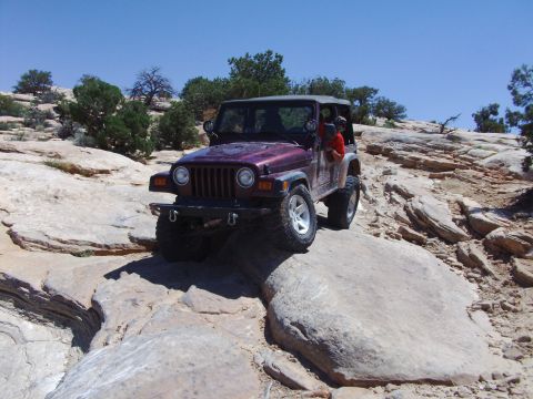 1995 Ford Bronco - A purple Jeep Wrangler TJ navigates a challenging rocky terrain under a clear blue sky.