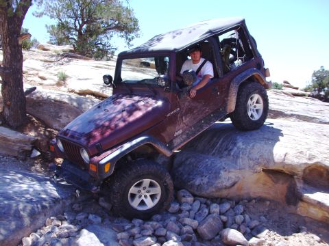 1995 Ford Bronco - A maroon Jeep Wrangler TJ navigates a rocky trail, demonstrating its off-road capabilities.
