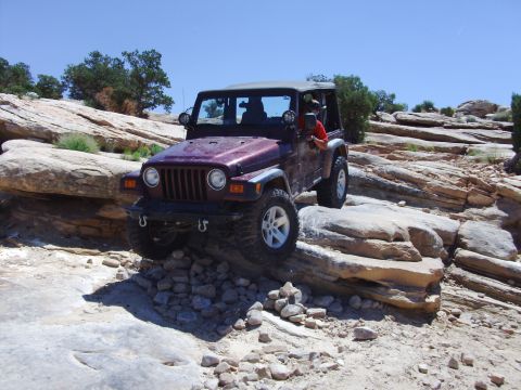 1995 Ford Bronco - A Jeep Wrangler TJ navigates a rocky off-road course under a clear blue sky.