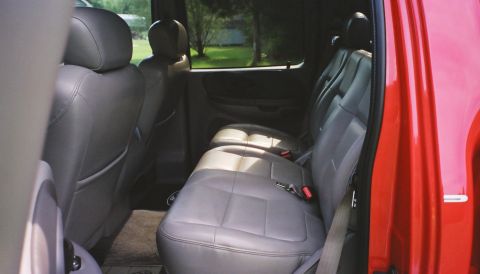 2007 Ford Mustang - The rear interior of a red truck shows gray leather seats and seatbelts.