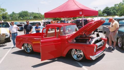 2007 Ford Mustang - Classic red Ford F-100 pickup truck displayed with its hood open at a car show.