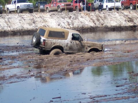 1992 Ford Bronco - A muddy Ford Bronco is stuck in a water-filled ditch while other vehicles watch from the bank.
