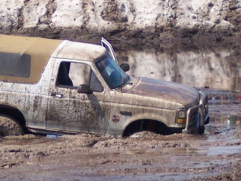 1992 Ford Bronco - A 1992 Ford Bronco is stuck in thick mud with its driver's door ajar.