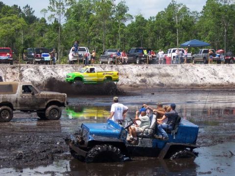 1992 Ford Bronco - A muddy 1992 Ford Bronco navigates a challenging off-road course with other vehicles and spectators present.