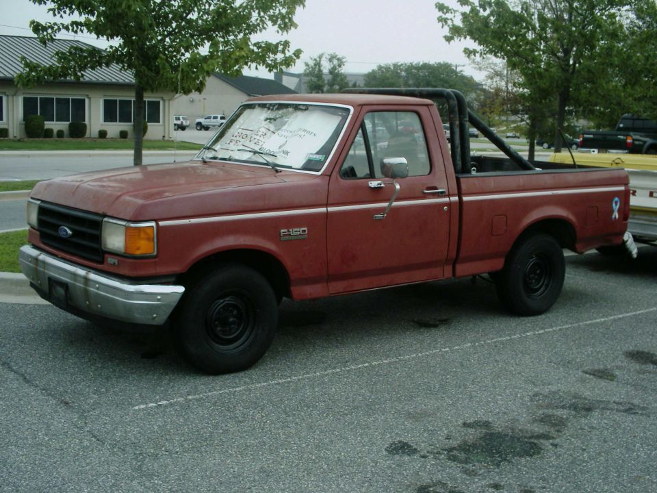 Red Ford F-150 pickup with bed bars parked in a lot, side view