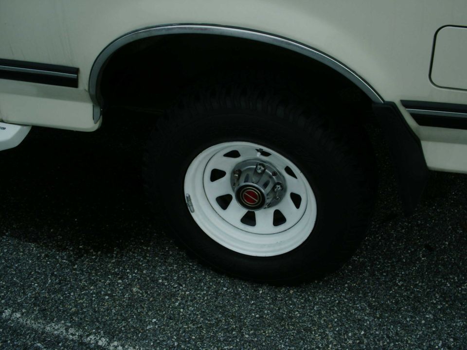 White eight-slot steel wheel and all-terrain tire on a cream truck body