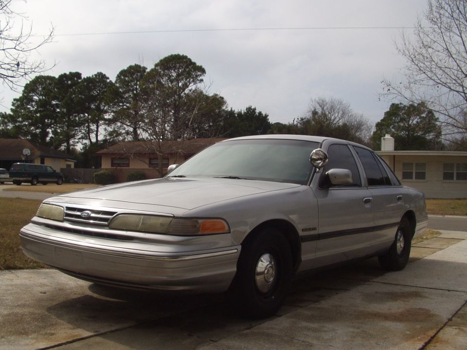Silver Ford Crown Victoria sedan with A-pillar spotlight and black steel wheels parked in a driveway