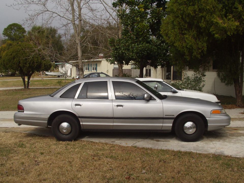 Silver Ford Crown Victoria sedan, side view, parked in a residential driveway with plain steel wheels and hubcaps
