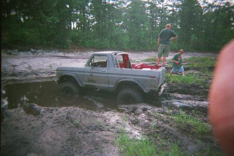 1990 Ford Bronco - A classic Ford Bronco is stuck in the mud while two onlookers observe the situation.