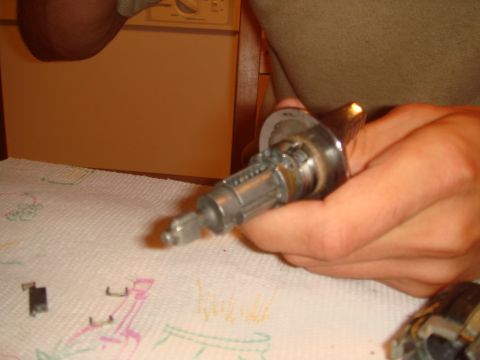 1992 Ford Bronco - Close-up of an ignition lock cylinder and housing being held, with small parts on a paper towel.