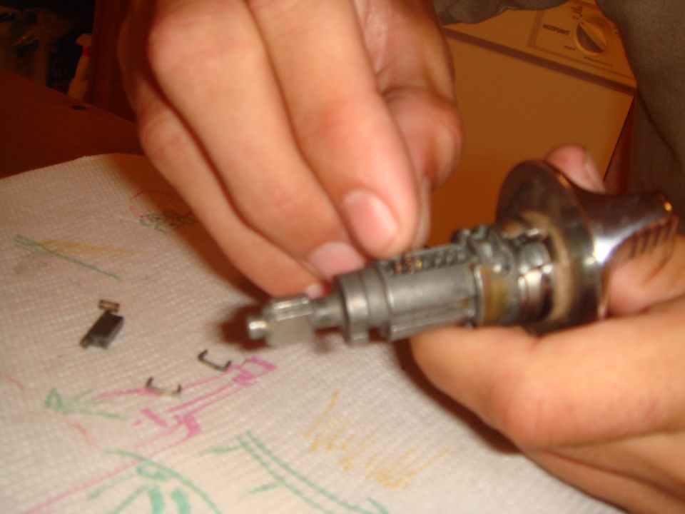 Hands working on a disassembled ignition lock cylinder with small parts on a paper towel