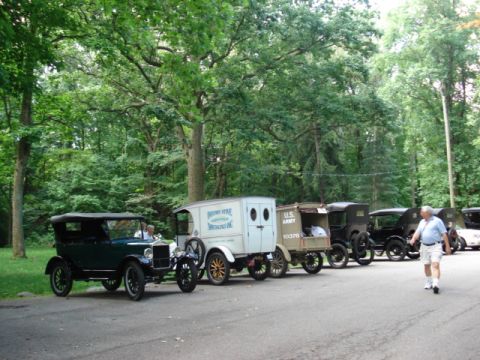 1909 Ford Model T - A line of antique vehicles, including a U.S. Army truck, are parked outdoors near a wooded area.