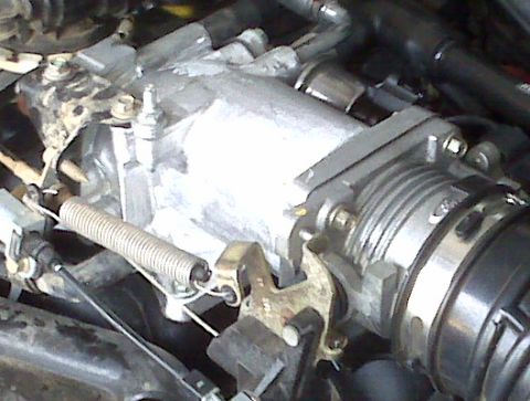2004 Ford Crown Victoria - Close-up view of a vehicle's throttle body assembly, showing mechanical linkages and a return spring.