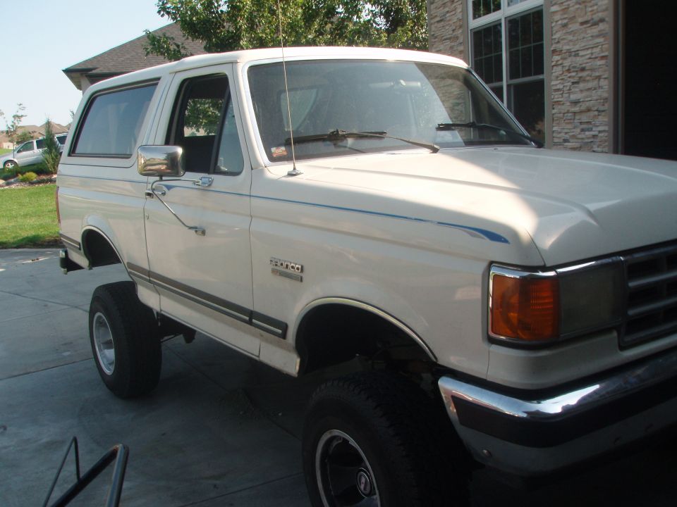 White 1987 Ford Bronco with lifted suspension and blue pinstripes