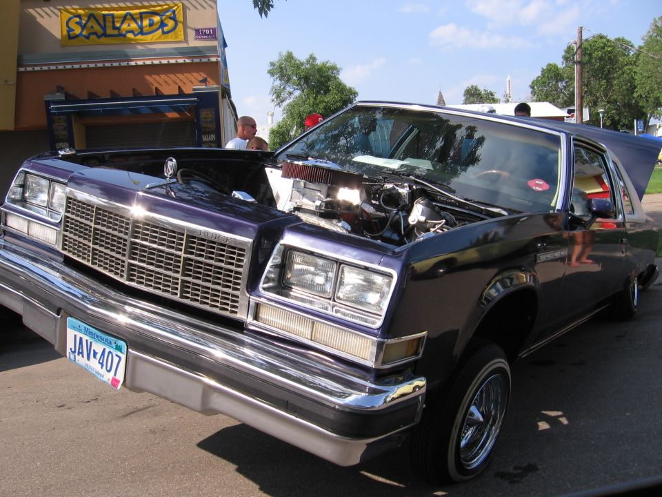 Purple Buick Regal with hood open, showing engine and chrome grille. Lowrider stance with wire wheels