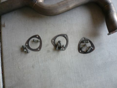 1996 Ford Probe - Exhaust pipe and associated gaskets and bolts are laid out on a concrete surface.