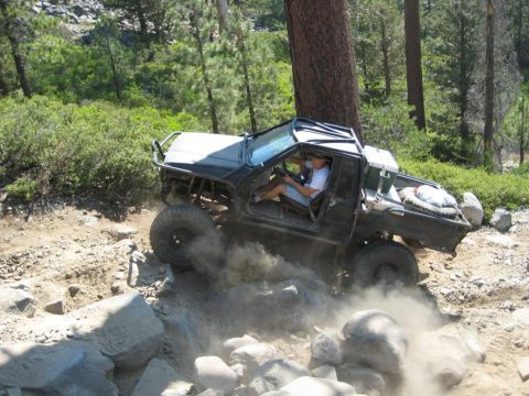 1999 Jeep Grand Cherokee - Off-road truck navigates a challenging rocky trail, creating dust clouds.