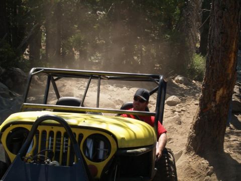 1999 Jeep Grand Cherokee - A man drives a yellow off-road buggy through a dusty, wooded trail with large rocks.