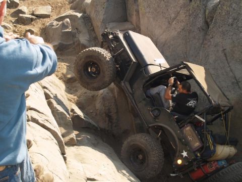 1999 Jeep Grand Cherokee - An off-road vehicle is precariously positioned on a steep, rocky terrain, with a person outside the vehicle appearing to guide it.