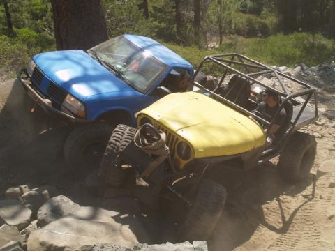 1999 Jeep Grand Cherokee - Two modified off-road vehicles tackle a challenging rocky trail in a wooded area.