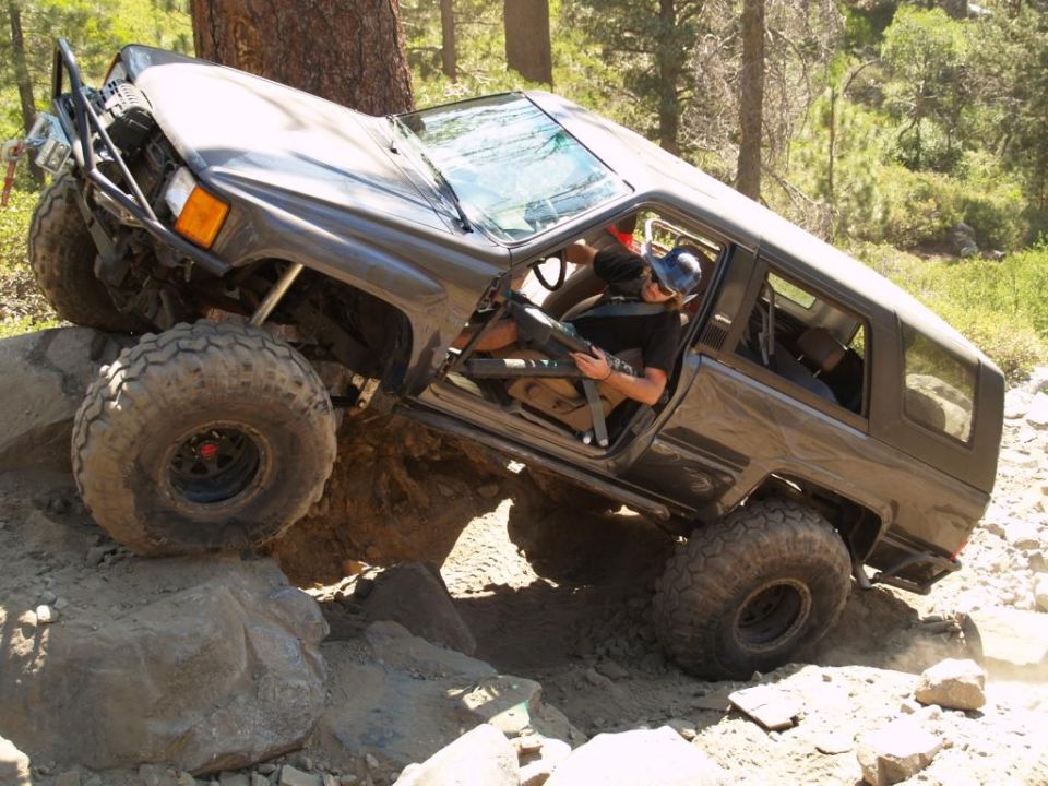 Dark gray off-road SUV with large tires climbing over rocks, driver visible inside