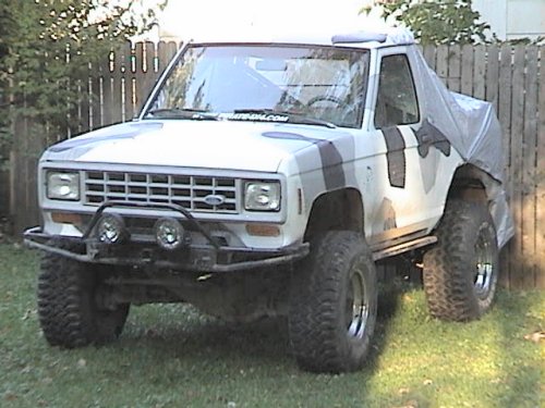 White chopped-top lifted Ford SUV with brush guard and big tires on grass by fence