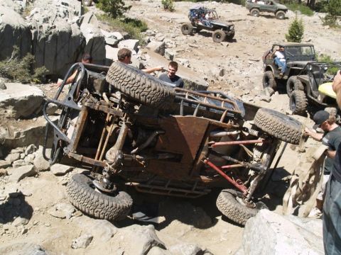 1999 Jeep Grand Cherokee - An off-road vehicle has tipped onto its side while navigating a rocky trail, with several people observing and assisting.