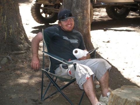 1999 Jeep Grand Cherokee - A man relaxes in a camping chair outdoors, holding a roll of toilet paper.