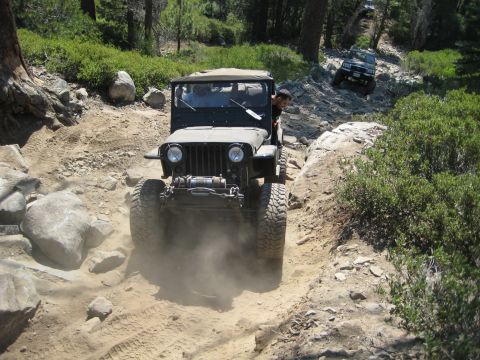 1999 Jeep Grand Cherokee - Two Jeeps navigate a challenging off-road trail in a wooded area.