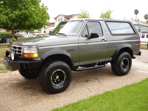 1994 Ford Bronco - This gray Ford Bronco is shown from a three-quarter front angle, highlighting its aftermarket modifications.