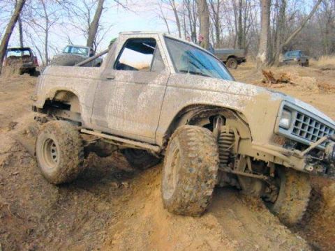 1987 Ford Bronco II - This off-road vehicle is covered in mud while navigating a steep, dirt incline with other vehicles nearby.