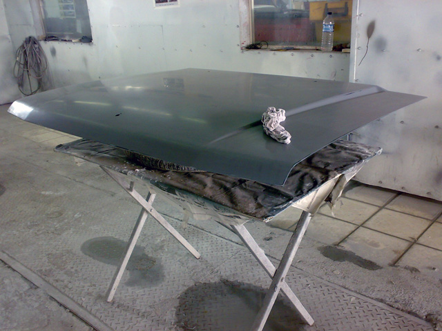 Freshly painted dark green hood on trestle stands in a spray booth