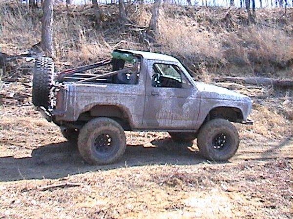 Muddy topless lifted Ford Bronco II on off-road tires, side view on dirt trail